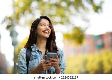 Portrait happy young woman holding mobile phone outdoors  - Shutterstock ID 2224332119