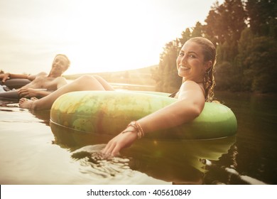 Portrait of happy young woman in lake on inflatable ring with her boyfriends in background. Young couple relaxing in water on a summer day. - Powered by Shutterstock