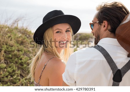 Portrait of happy young woman looking at camera. Cheerful woman wearing black straw hat while going at beach. Close up face of smiling girl with her boyfriend outdoor.
