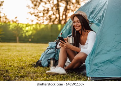 Portrait Of A Happy Young Woman On Summer Camping Trip, Sitting In Tent And Using Smart Phone.