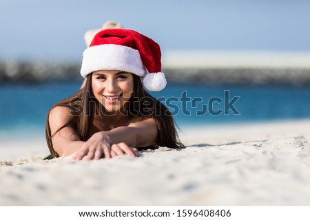 Portrait of happy young woman on tropical beach wearing Santa hat enjoying winter holidays in exotic destination.