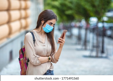 Portrait Of A Happy Young Woman Outdoors Wearing A Facemask While Texting On Her Cell Phone - Pandemic Lifestyle Concepts. Young Woman Wearing A Face Mask