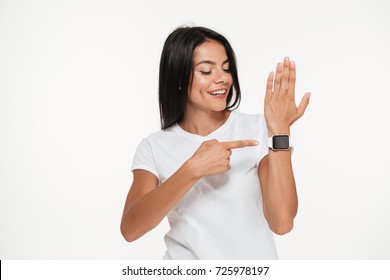 Portrait of a happy young woman pointing finger at smart watch on her wrist isolated over white background