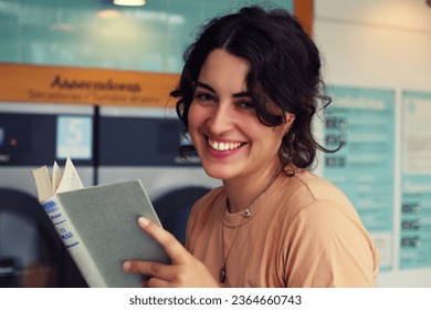 Portrait of a happy young woman reading a book at the laundromat - Powered by Shutterstock