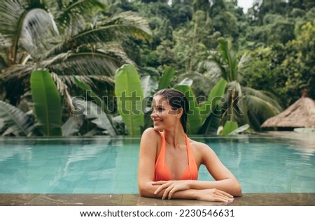 Portrait of happy young woman relaxing in swimming pool. Woman standing in pool of luxury holiday resort.