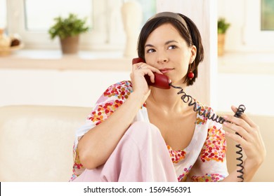 Portrait Of Happy Young Woman Sitting On Sofa At Home, Talking On Landline Phone.