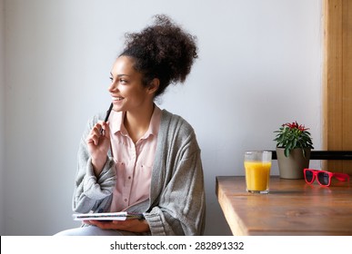 Portrait Of A Happy Young Woman Sitting At Home With Pen And Paper