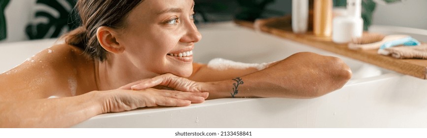 Portrait of happy young woman smiling aside while resting in bathtub at luxury spa resort. Wellness, beauty and care concept