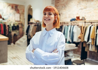 Portrait Of A Happy Young Woman Standing With Her Arms Crossed In Her Fashion Retail Store. Trendy Female Boutique Owner Looking At Camera And Smiling.