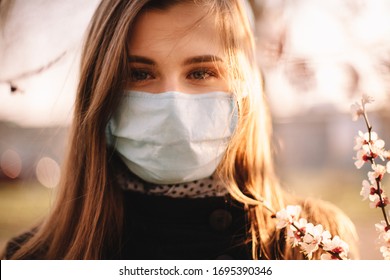 Portrait Of Happy Young Woman Wearing Face Medical Mask Standing By Flowering Tree In Spring