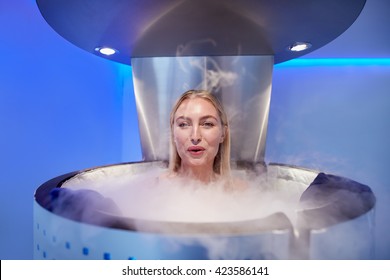 Portrait of happy young woman in a whole body cryotherapy cabin. She is looking at camera and smiling.