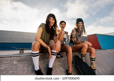 Portrait of happy young women sitting on ramp at skate park and smiling. Group of female friends at skate park. - Powered by Shutterstock