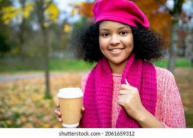 Portrait of a happy youth. A dark-skinned black woman in an autumn park holds a glass of glass coffee to her. Close-up, smiling and laughing African American girl on a walk.
