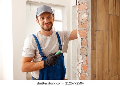 Portrait of hard working handyman or craftsman smiling at camera while filling the wall, preparing it for painting