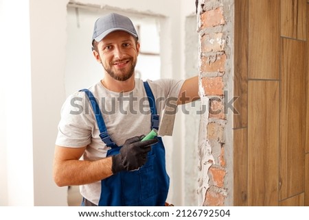 Portrait of hard working handyman or craftsman smiling at camera while filling the wall, preparing it for painting