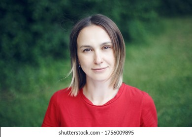 Portrait Head Shot Of Beautiful Pensive Caucasian Middle Age Woman With Long Light Bob Hair. Casual Style Real Person In Red T-shirt. Closeup Face Of Happy Calm Woman In Park Outside Nature. 