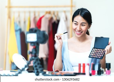 Portrait Or Headshot Of Attractive Young Asian Influencer, Beauty Blogger, Content Creator Or Vlogger Girl Review Make Up Looking At Camera At Home. Asian Woman Using Internet For Tutorial Live Video.