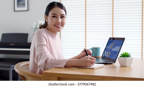 Portrait Headshot Young Attractive Beautiful Asia Female Sit On Desk Smile To Camera Work At Home Remotely Computer Laptop Job. College Student, Employee Feel Cozy Happy In Weekend Work Life Balance.