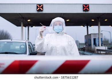 Portrait Of Health Care Medical Worker In Protective White Suit Standing At Border Crossing Checkpoint To Preform PCR Test On Passengers Due To Corona Virus Pandemic.