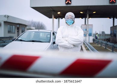 Portrait Of Health Care Medical Worker In Protective White Suit Standing At Border Crossing Checkpoint To Preform PCR Test On Passengers Due To Corona Virus Pandemic.