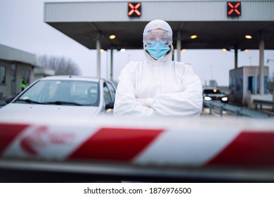 Portrait Of Health Care Medical Worker In Protective White Suit Standing At Border Crossing Checkpoint To Preform PCR Test On Passengers Due To Corona Virus Pandemic.