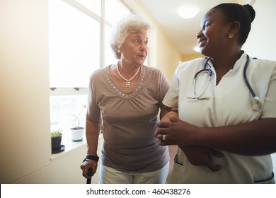 Portrait Of Healthcare Worker And Senior Woman Walking Together. Nurse Assisting Senior Female Patient While Walking In Nursing Home.