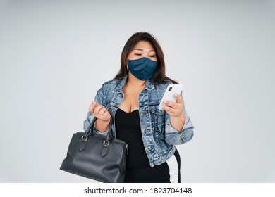 Portrait Of Healthy Asian Chubby Woman Wear Mask And Jeans Jacket Using Smartphone For Online Shopping Over White Background.