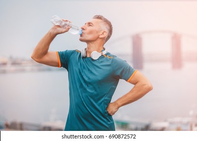 Portrait of healthy athletic middle aged man with fit body holding bottle of refreshing water, resting after workout or running. middle aged male with a drink after outdoor training. 