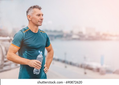 Portrait of healthy athletic middle aged man with fit body holding bottle of refreshing water, resting after workout or running. middle aged male with a drink after outdoor training. 