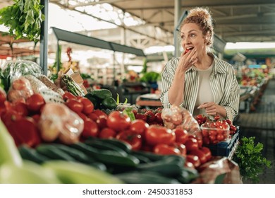 Portrait of a healthy female customer standing at farmer's market near market stall and trying out fresh organic cherry tomato. Young blond shopper biting raw vegetables at greengrocery marketplace. - Powered by Shutterstock