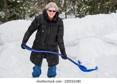 A Portrait Of A Healthy Senior Woman Holding A Shovel Full Of Snow On A Cold Snowy Day.  