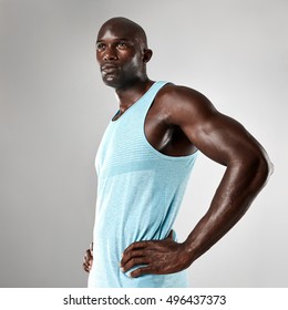 Portrait Of Healthy Young Black Man With Muscular Body Standing Against Grey Background. Afro American Fitness Model With Hands On Hips And Looking Away.