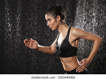 Portrait of a healthy young sportswoman running under the rain over black background - Powered by Shutterstock