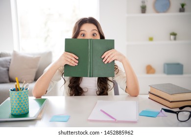 Portrait of her she nice attractive charming cute cheerful cheery funny wavy-haired pre-teen girl hiding behind materials class work in light white interior room library indoors