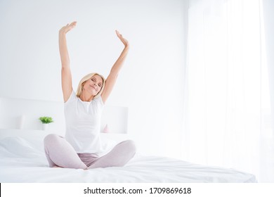 Portrait Of Her She Nice Attractive Lovely Dreamy Cheery Senior Woman Sitting In Bed Stretching Waking Up Fresh Start Yoga Practicing In Modern Light White Interior Room Flat Apartment Indoors