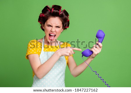 Portrait of her she nice attractive fashionable glamorous evil mad fury wife wearing curlers holding in hands showing headset yelling bad mood isolated over green color background