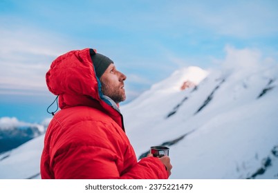Portrait of high altitude mountaineer dressed red warm dawn jacket holding metal mug of hot tea thinking and enjoying fresh mountains frosty air. Mera Peak High Camp 5700m, Himalayas, Nepal.