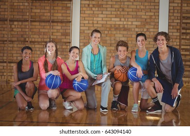 Portrait Of High School Kids And Coach Kneeling With Basketball In The Court