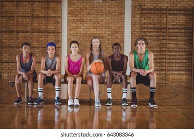 Portrait Of High School Kids Sitting On A Bench In Basketball Court