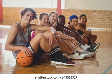 Portrait Of High School Kids Sitting On The Floor In Basketball Court Indoors