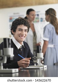 Portrait Of High School Student Using Microscope And Taking Notes In Laboratory