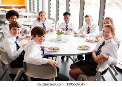 Portrait Of High School Students Wearing Uniform Sitting Around Table And Eating Lunch In Cafeteria