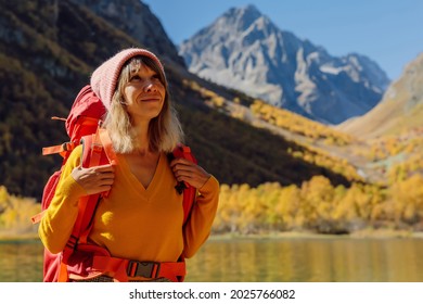 Portrait of hiker happy woman at lake in the autumnal mountains. Mountain lake and tourist