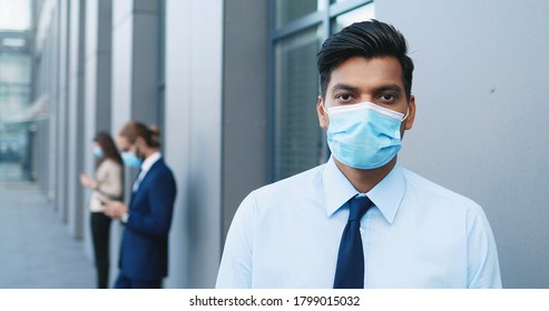 Portrait Of Hindu Young Handsome Businessman Standing At Street And Looking At Camera. Man From India In Tie And Medical Mask Outside Business Center. Social Distance. Close Up. Covid-19.