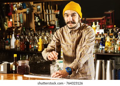 Portrait Of Hipster Barman Mixing A Cocktail With A Spoon At Bar Background.