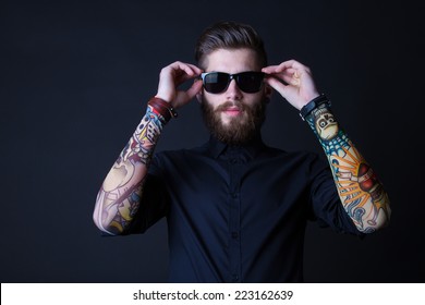 portrait of a hipster man wearing colourful tattooes on his arms posing over a  black background