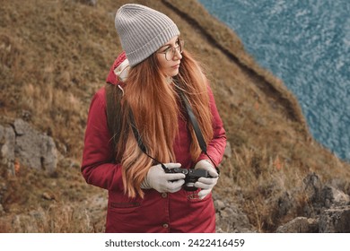Portrait of a hipster woman in glasses and autumn outfit holding camera in hands, looking for a good shot. Solo traveler, explorer, freelance photographer concept