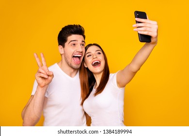 Portrait of his he her she two nice attractive lovely stylish trendy cheerful positive people making taking selfie enjoying showing v-sign isolated over vivid shine bright yellow background