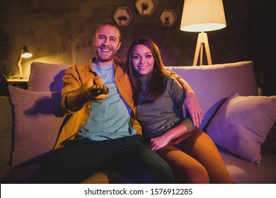 Portrait of his he her she nice attractive lovely cheerful cheery couple sitting on divan watching TV resting embracing at home house apartment living-room indoors