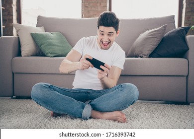 Portrait of his he nice attractive crazy addicted glad cheerful cheery guy sitting on carpet using cell playing game having fun at modern industrial loft brick interior style living-room - Shutterstock ID 1716393742